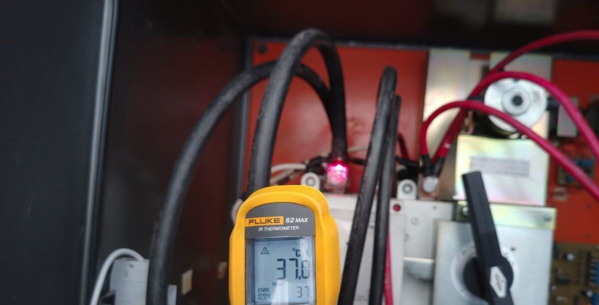 Técnico midiendo temperatura con termómetro infrarrojo en un tablero